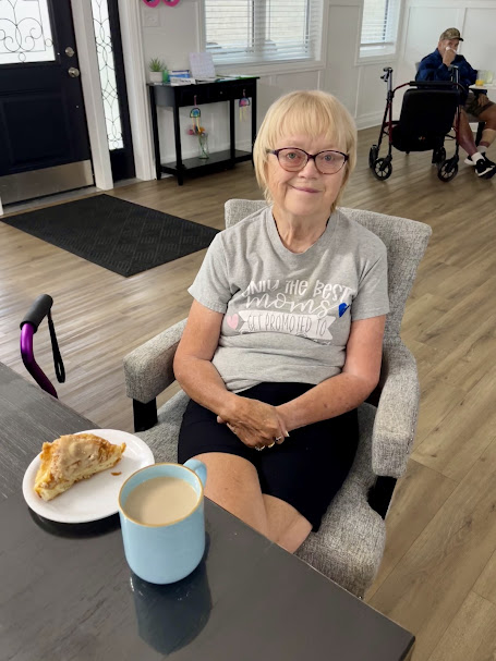 Senior woman seated safely in an assisted living lounge with coffee, showing a supportive environment to prevent falls.