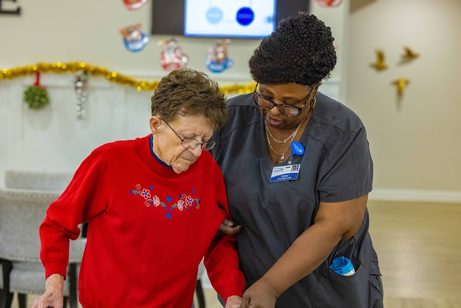Caregiver helping an elderly woman walk inside an assisted living community in Indiana.